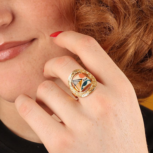 Image of model wearing quirky round ring with hand painted multicolour motif in centre on gold metal finish.
