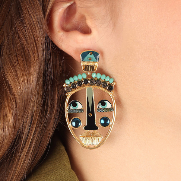 Image of model wearing stud earrings with big quirky eyes and mouth face feature surrounded with blue stones and beads.